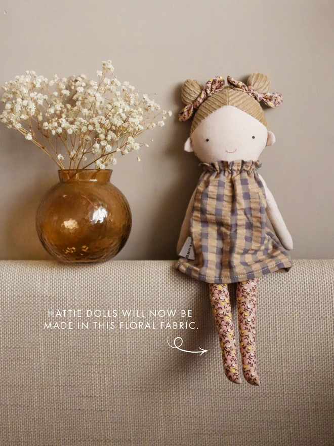 textile doll with beige and grey gingham dress and brown floral dress with double knot hairstyle