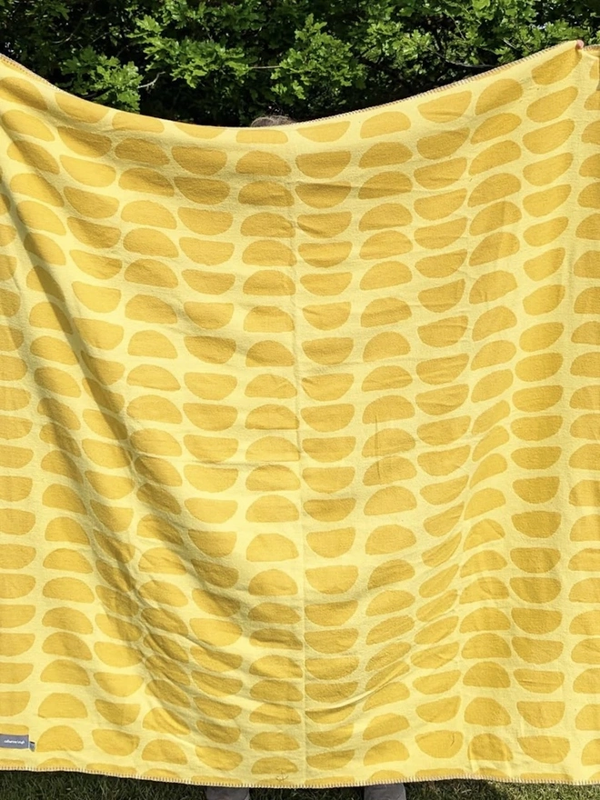 Organic Cotton Throw, a person holding the throw in front of them outside. 