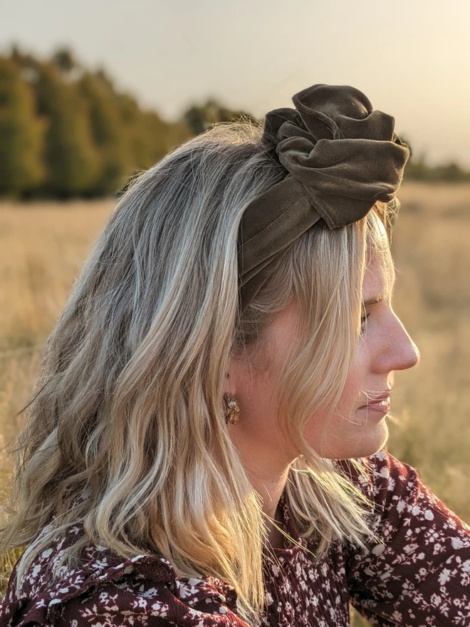 A caper green velvet fabric headband on a woman with blonde hair.