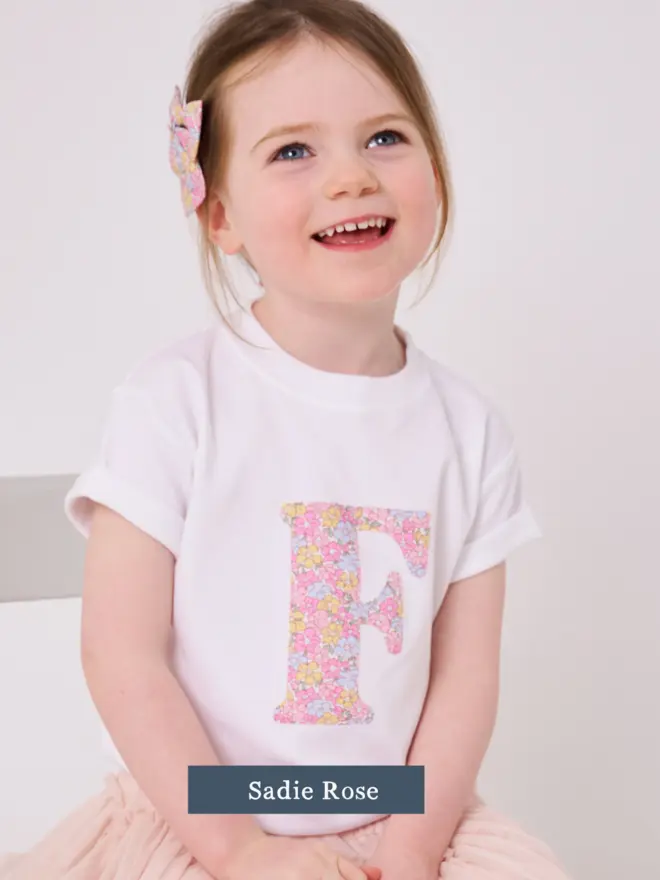 a 3 year old girl wearing a personalised kids white t-shirt with an initial cut from sadie rose liberty floral print on the front