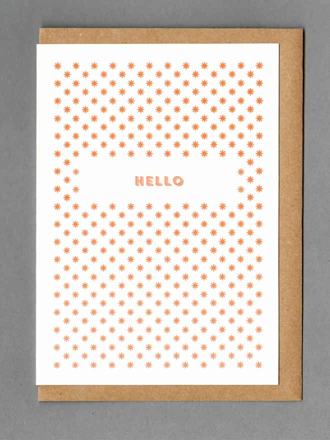 White card with orange stars and orange text reading 'Hello' with a brown envelope behind it