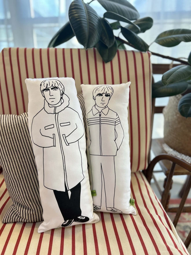 Black and white illustrated screen printed cushion of Oasis band members Liam and Noel Gallagher. The cushions sit on a striped sofa.
