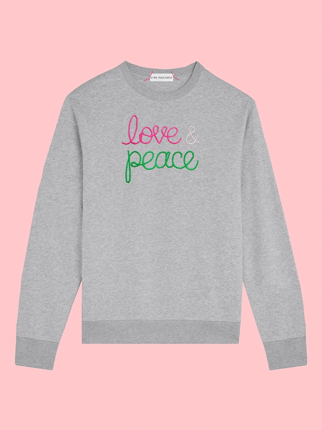 Grey sweatshirt embroidered with the words love & peace on a pink background