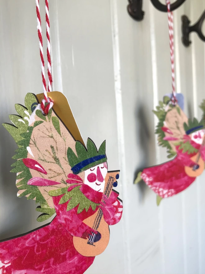 Red and green illustrated angel decoration by Esther Kent, hangs from red and white striped string