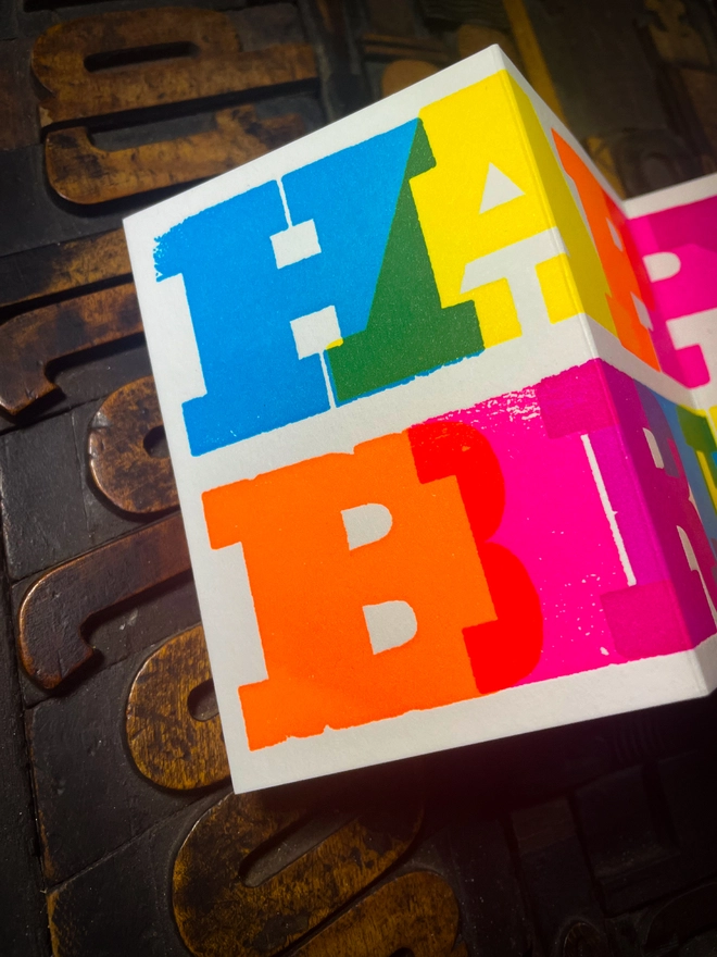 Artisan letterpress printed "Happy Birthday" concertina card featuring bold typography in six fluorescent inks with a deep impression print