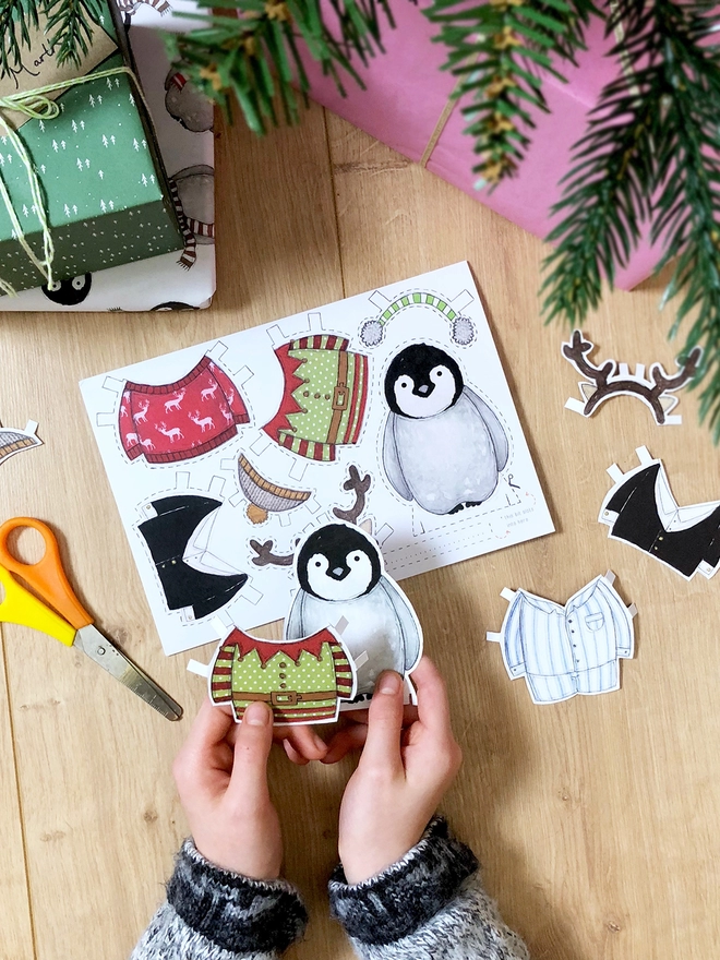 A child is playing with a dress up penguin paper doll that has been cut from a Christmas greetings card.