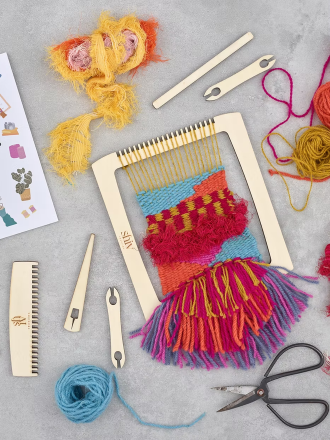 beginners' weaving kit. a wooden weaving kit and colourful yarn displayed on a white backdrop.