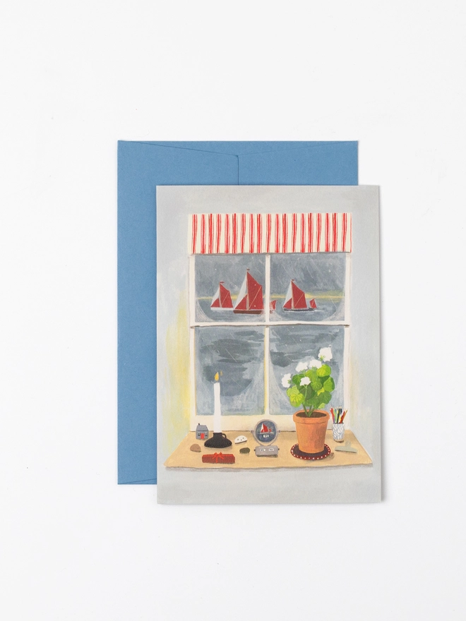 a greeting card featuring an illustration of a view out of a window. The windowsill inside is covered in trinkets, a burning candle and a white geranium. The view outside is of three sailing ships on a dark winter's morning.