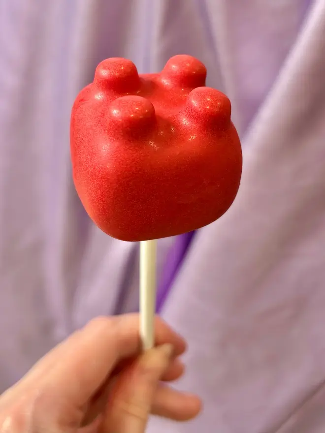 lego cake pop. a red lego brick cake pop on a stick.