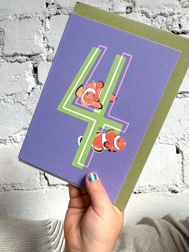 a purple card with a big green number 4 and two clown fish illustrations and a green envelope
