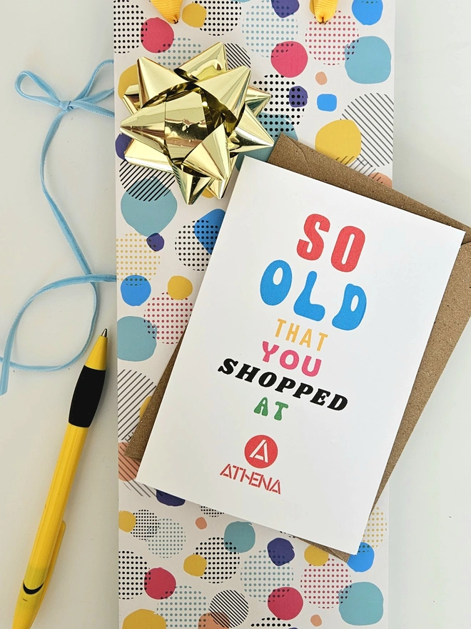 A photograph of the front of a humorous A6 greeting card illustrated using brightly coloured text and the retro shop logo. The text says so old you shopped at Athena.