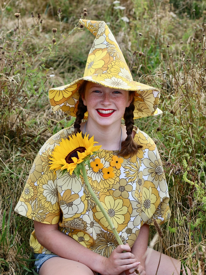 Funny looking girl smiling at camera with sunflower wearing handmade upcycled witch hat