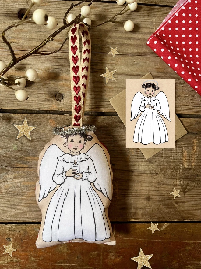 a sweet fabric angel decoartion printed fabric illustrated in a vinatge traditional style little angel with bunches holding a candle with a matching miniature greeting acrd and kraft envelope