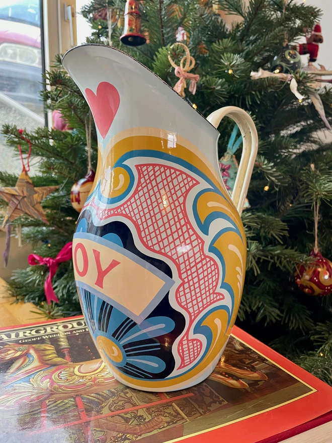 Blue enamel jug hand painted with a fairground design in blue, pink and yellow