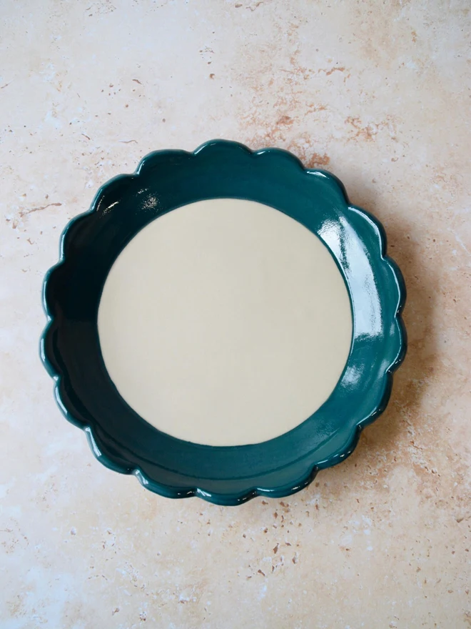Handmade ceramic plate with deep teal scalloped rim — full view from above