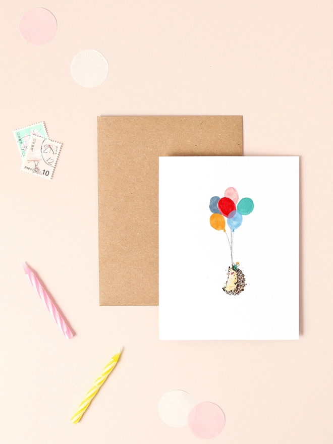 A delightful illustration of a hedgehog holding a bundle of colorful balloons, exuding a sense of joy and celebration. The hedgehog's cheerful expression and the vibrant hues of the balloons create a whimsical and festive atmosphere. The design is complemented by a soft, neutral background, enhancing the playful and heartwarming sentiment of the card.