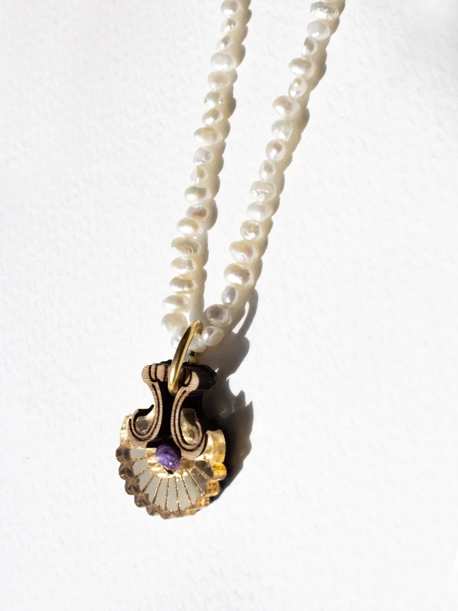Pearl necklace with a shell shaped gold pendant & gemstone on a white background