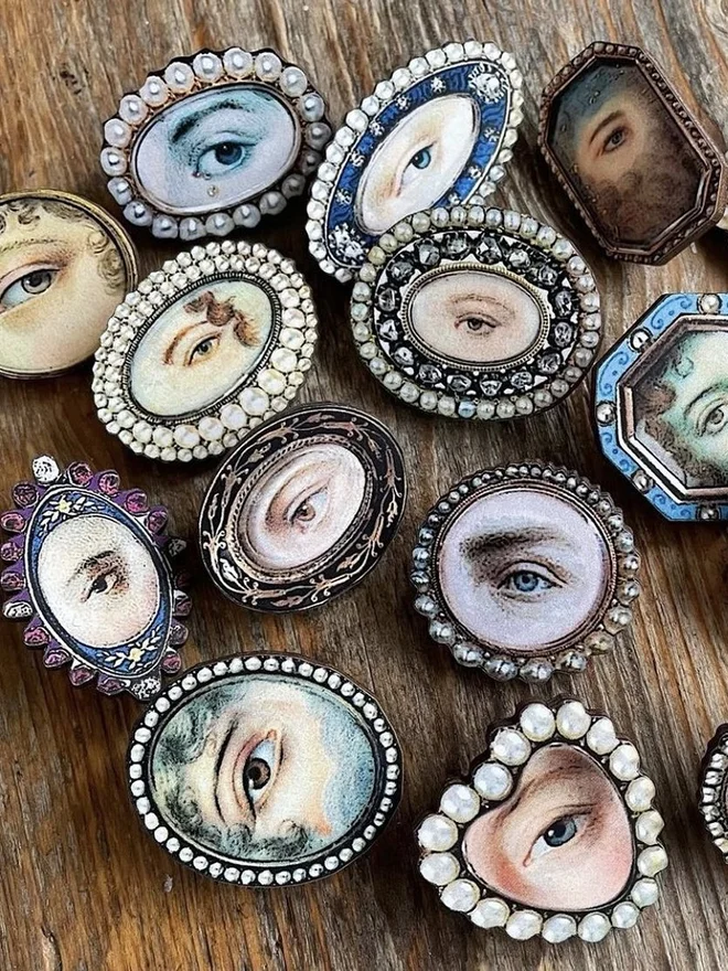 a collection of lovers eyes brooches laid out on a vintage wooden surface