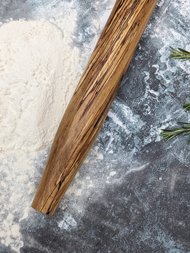 Close up of a stunning hand made rolling pin in Spalted Beech by Something From The Turnery, the picture is focussed on the darker brown all natural detailing along one end of the rolling pin.
