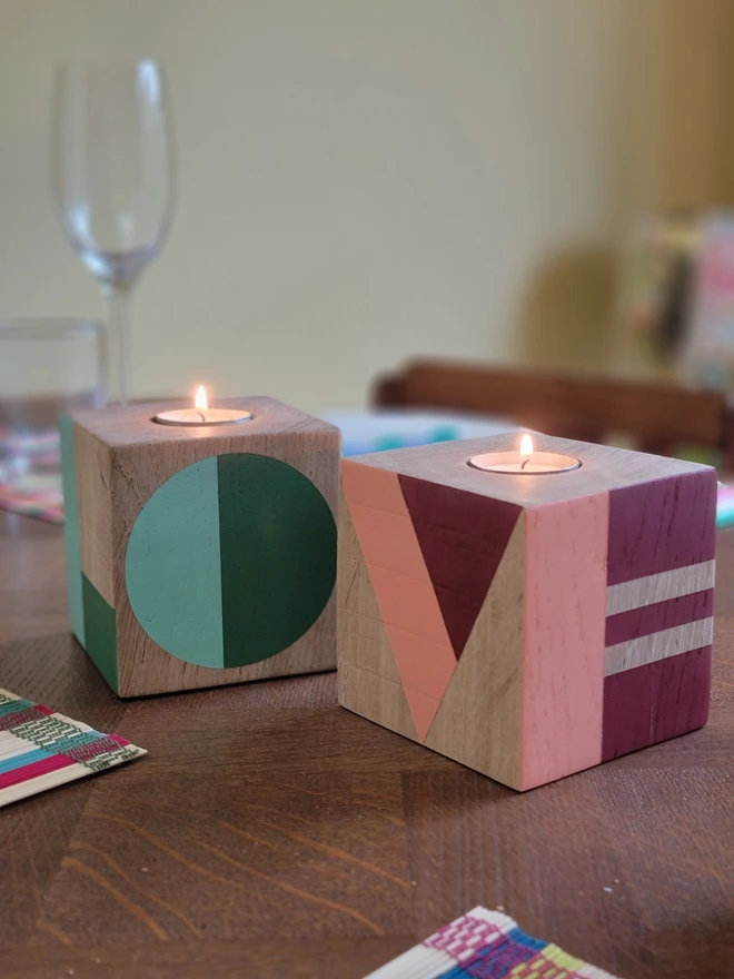 Two wooden cube painted tealight holders on a dining table