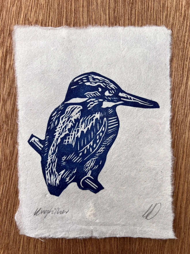 Hand-printed blue kingfisher lino print on natural handmade paper, featuring a bold graphic illustration of a kingfisher.