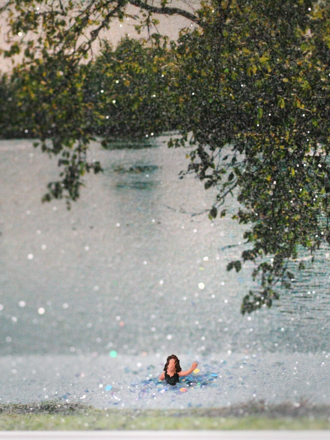 Artbox comprising a tiny woman swimming against sparkling river backdrop (close up)