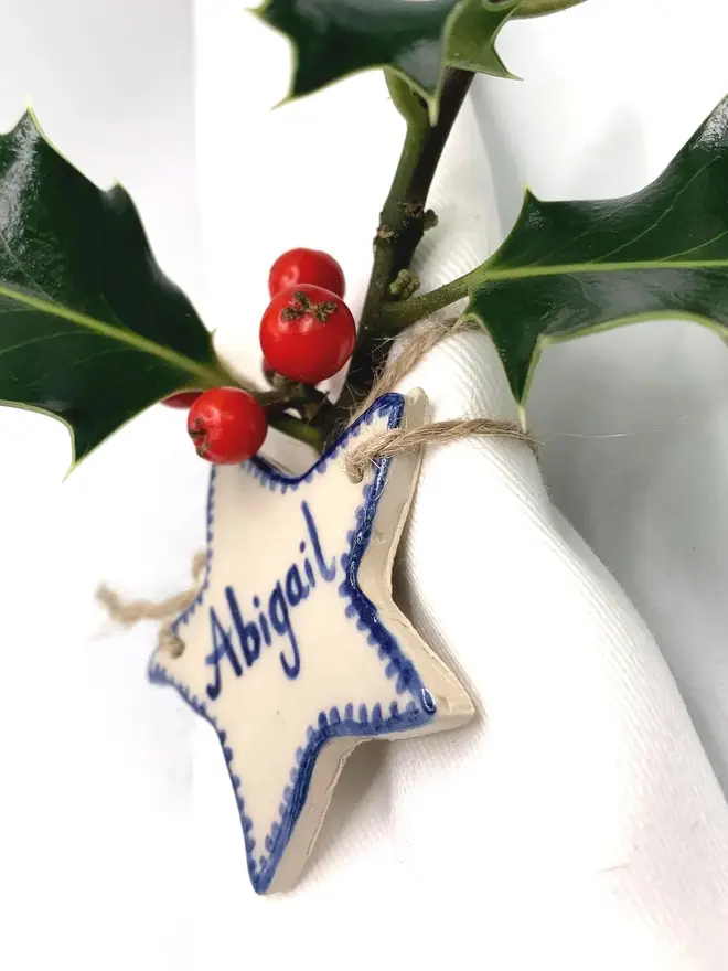 Personalised Ceramic Christmas Star Name Place Markers, a colourful ceramic start sitting on a white surface attached to a holly bush. 