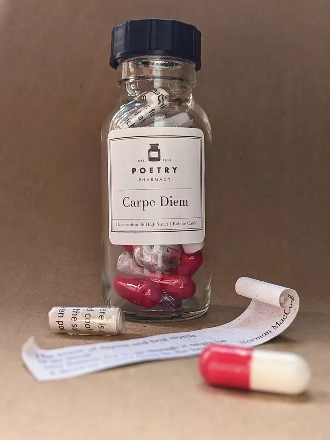 A bottle of Carpe Diem poetry pills, with one pill open to display the rolled banana paper quote it contains