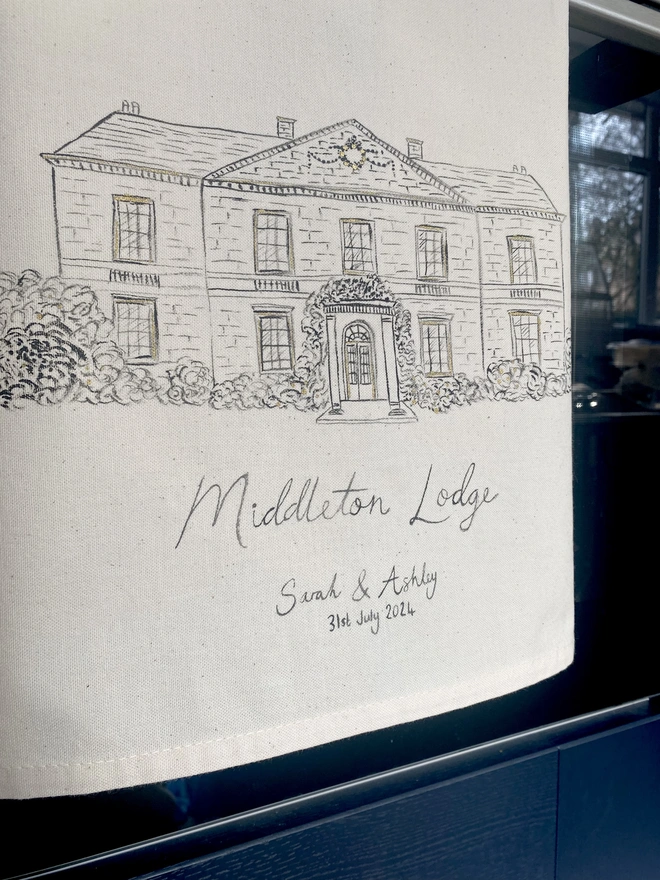 Tea towel with a hand painted venue illustration hanging on the handle of an oven