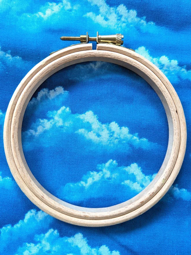 A wooden embroidery hoop lying on fabric with a cloud design