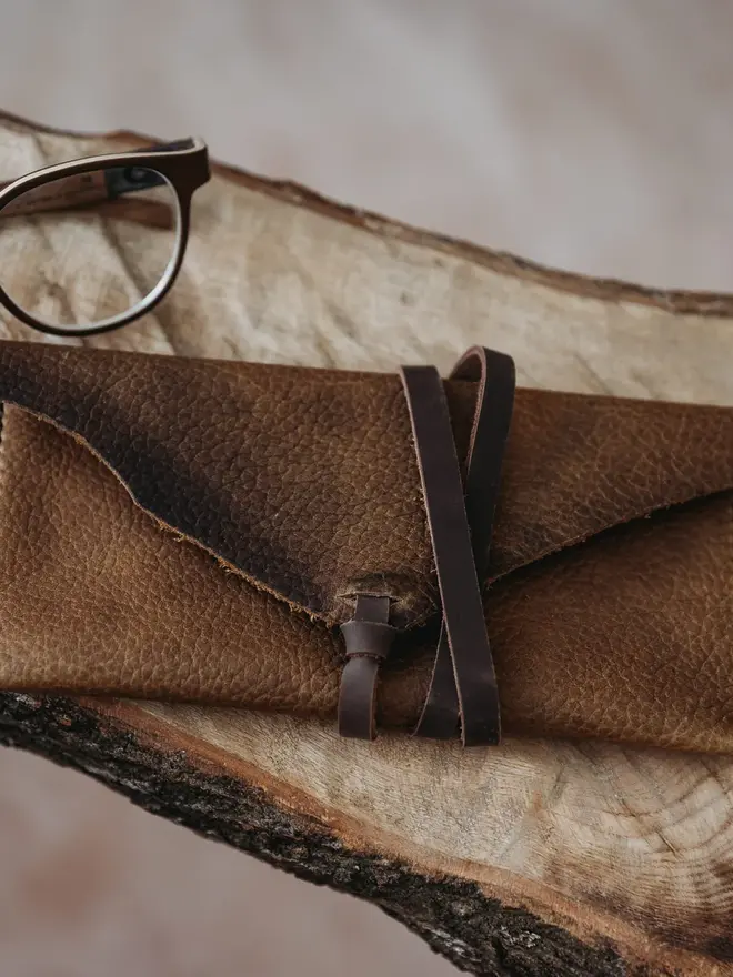 hand stitched leather pouch. a brown leather pouch on a cream cow hide background.