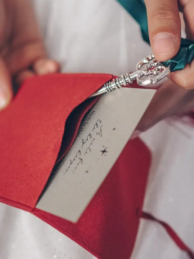 A close-up of the key's ornate silver bow slipping into the red pouch. The key keeper note card sits inside with it.