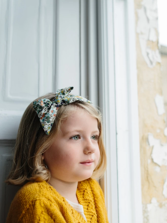 Little girl by a window wearing a liberty large bow alice band