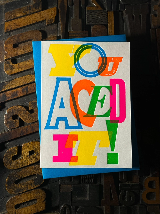 Colourful typographic letterpress card with bold overlapping neon letters spelling ‘You Aced It!’, perfect for celebrating exam success.