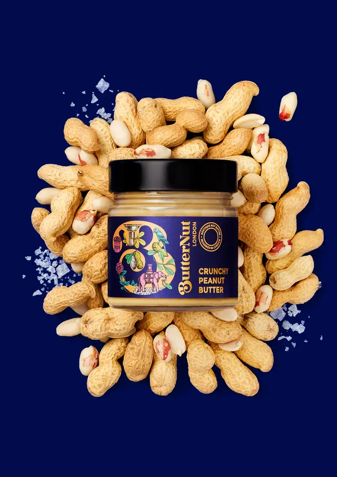crunchy peanut butter. a jar of peanut butter photographed against a dark blue background surrounded by peanuts.