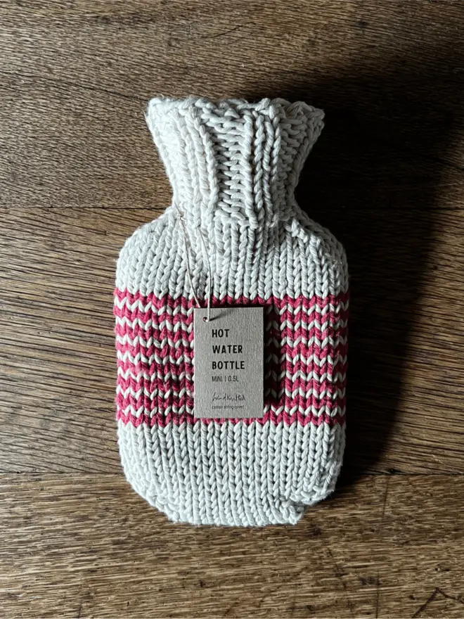 Mini Hot Water Bottle with red striped knitted string cover on an oak table