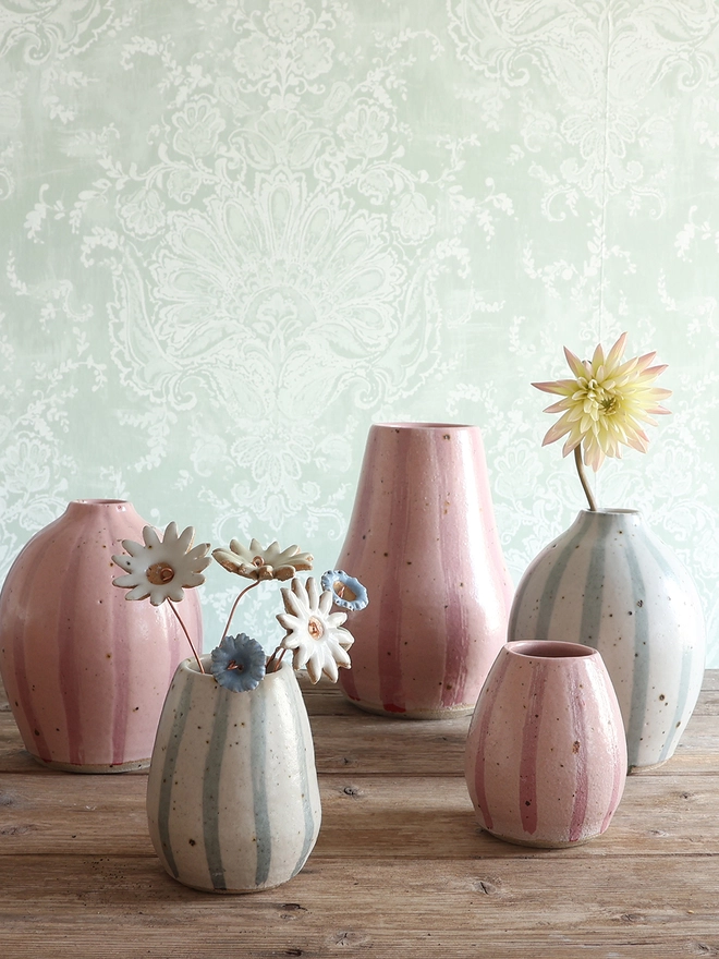 A collection of handmade ceramic vases in pink stripe and blue and white strips. The small vase in the foreground holds handmade ceramic flowers on copper wire stems