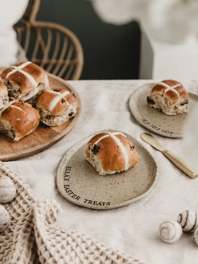 Hot cross bun on a ceramic egg plate with the personalised lettering Ella's Easter Treats