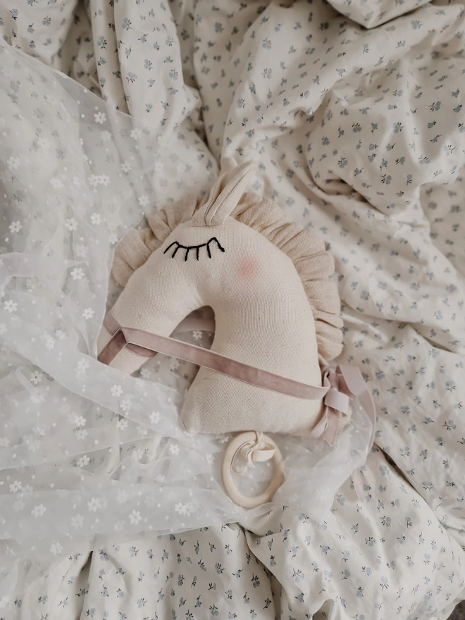 Horse Baby Rattle Toy, a horse rattle toy sitting on a child's bed surrounded by other accessories. 