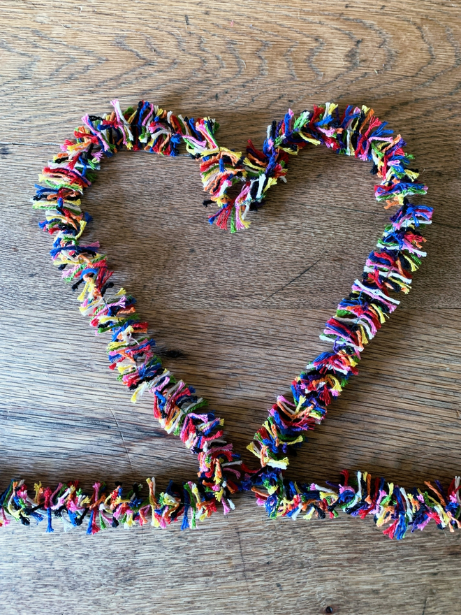 Rainbow Strinsel (plastic free multicolour string tinsel) forming a heart on an oak table
