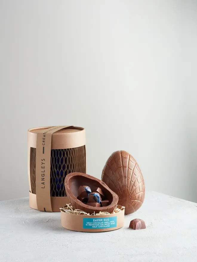 Extra Thick Milk Chocolate Easter Egg With Trevethan Gin, a chocolate egg sitting on a white surface. It is accompanied by another chocolate egg that is opened showing the chocolates within. 