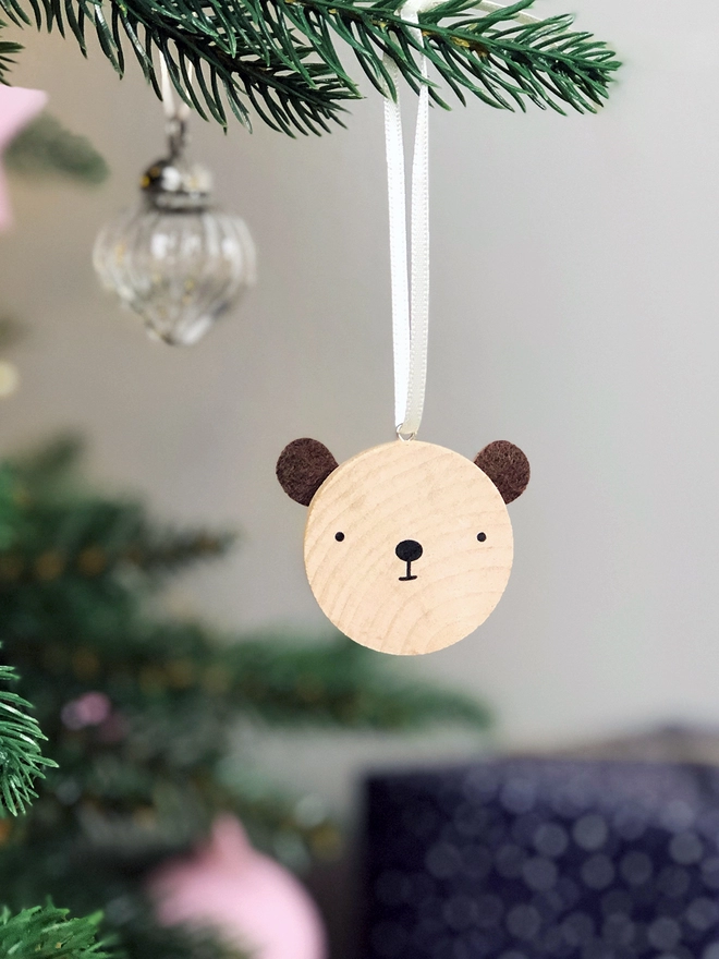 A small wooden and felt bear decoration hangs on a Christmas tree branch.