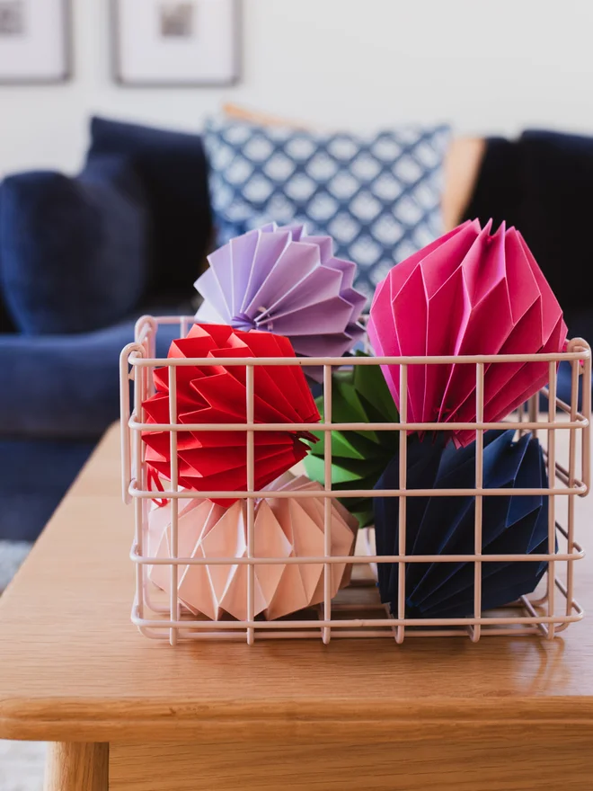 Paper origami shapes in a basket on a coffee table, with a sofa in the background.