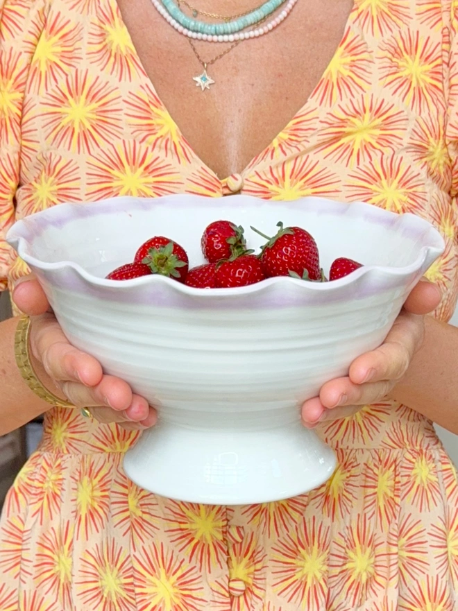Undulating hand thrown porcelain stem bowls with satin cream glaze and pink or turquoise rim on a rustic table top