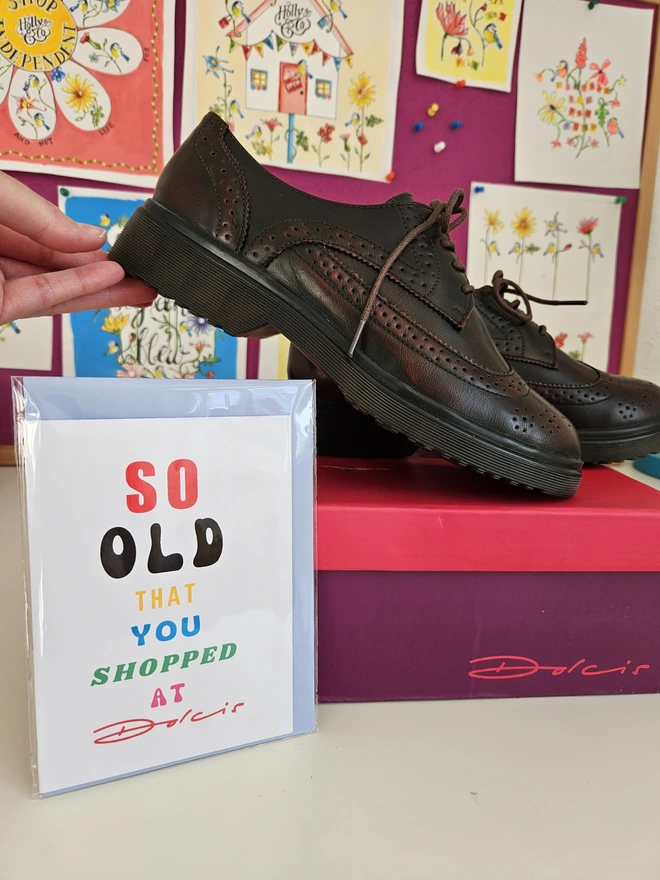 A photograph of the front of a humorous A6 greeting card illustrated using brightly coloured text and the retro shop logo. The text says so old you shopped at Dolcis next to a pair of shoes on a Dolcis shoe box 