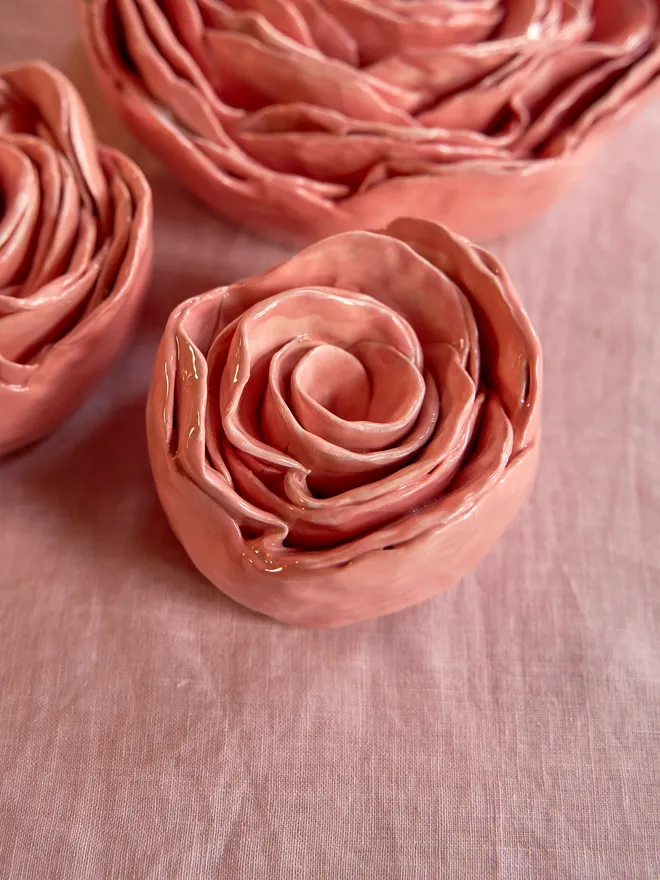 Small sized ceramic rose on a pale pink tablecloth surrounded by two other ceramic roses