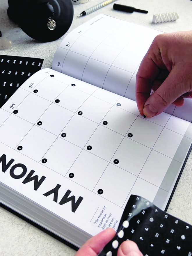 Hand sticking the Diary Date Dots into a month page of a Hello Time Planner