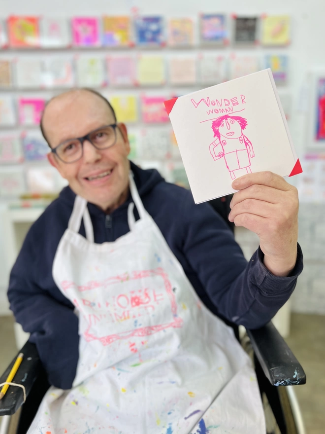 Artist holding the Wonderwoman charity card with a drawing of a woman in pink
