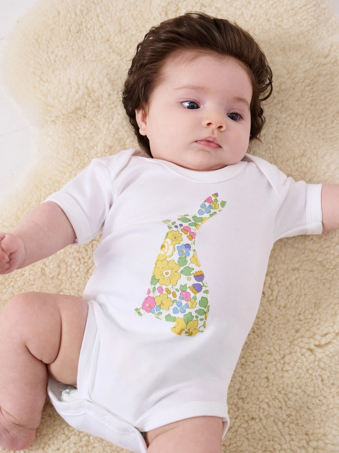 a baby wearing a cotton baby bodysuit babygrow with an easter bunny cut from yellow floral liberty print on the front 