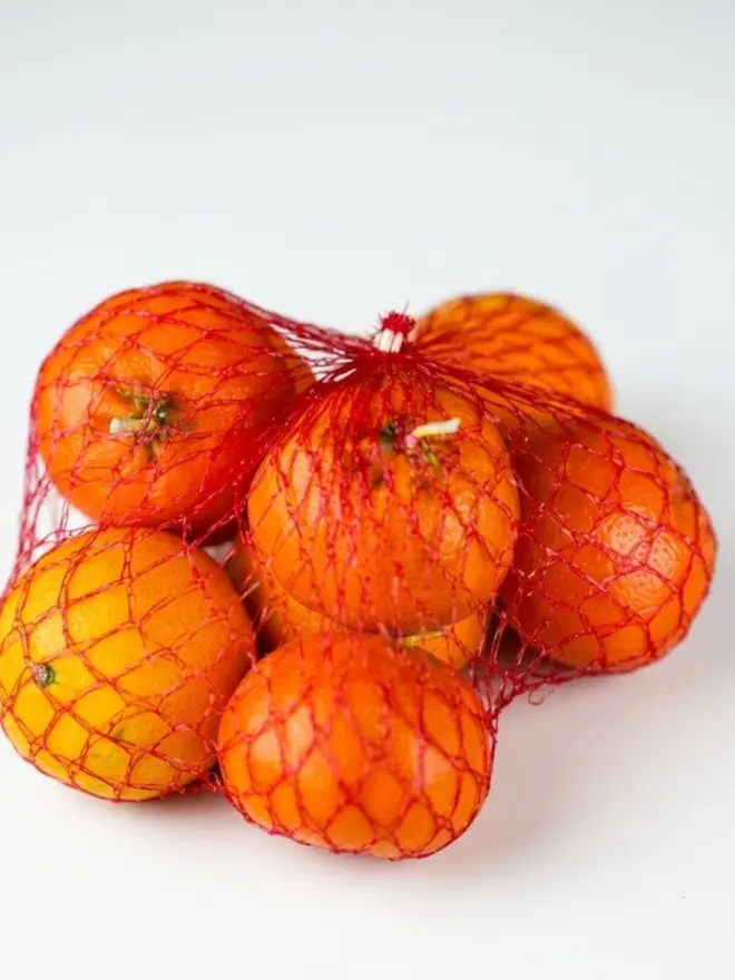 Christmas Satsuma Candle. a stack of candles shaped like satsuma oranges in red netting.